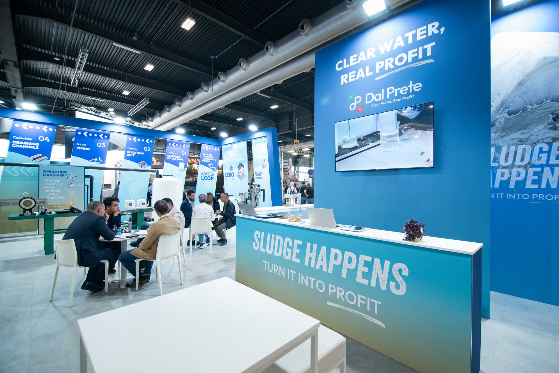 Desk reception dello stand Dal Prete a Marmomac con slogan "Sludge Happens" e luminosa area B2B visibile sullo sfondo.